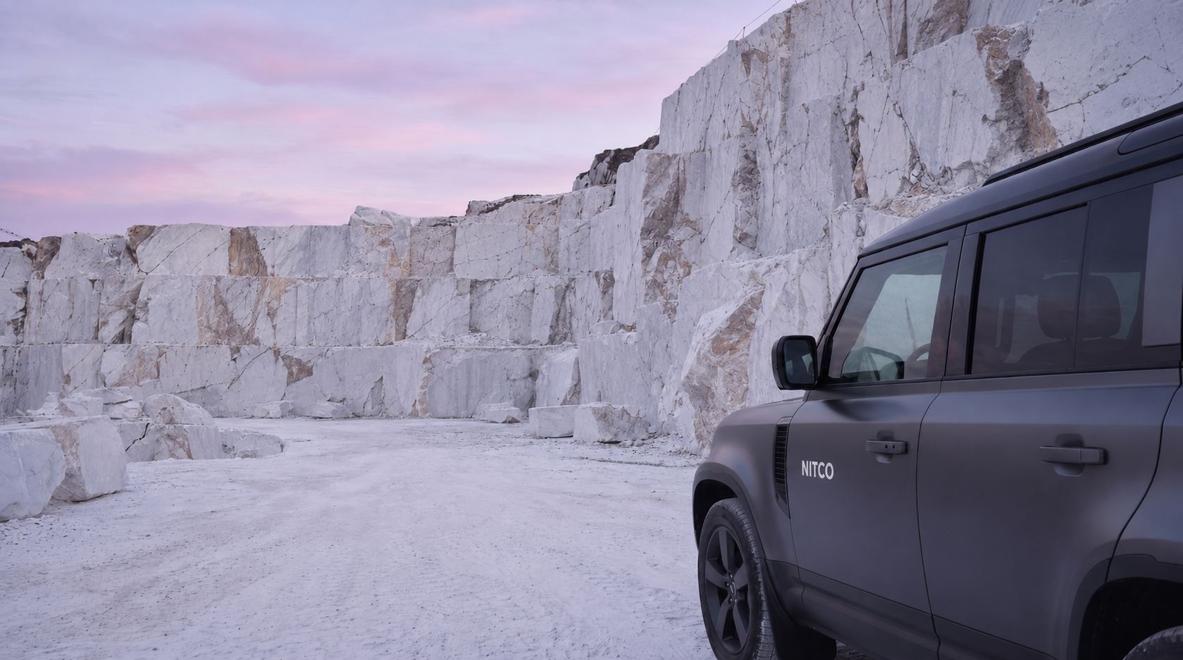 NITCO Defender at a marble quarry face at dawn, sheer white walls rising against a pink sky.